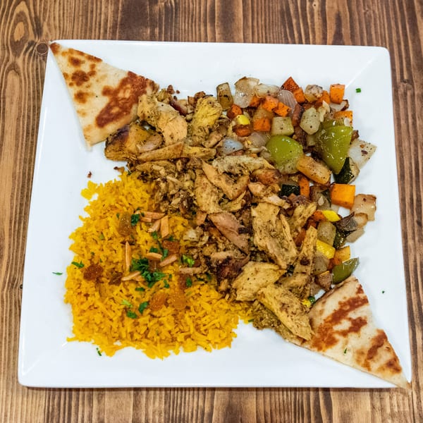 A white plate with chicken shawarma, yellow rice, roasted vegetables, and pita bread.