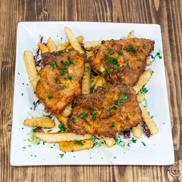 Three pieces of golden-brown fried chicken, french fries, and shredded cabbage on a white plate.