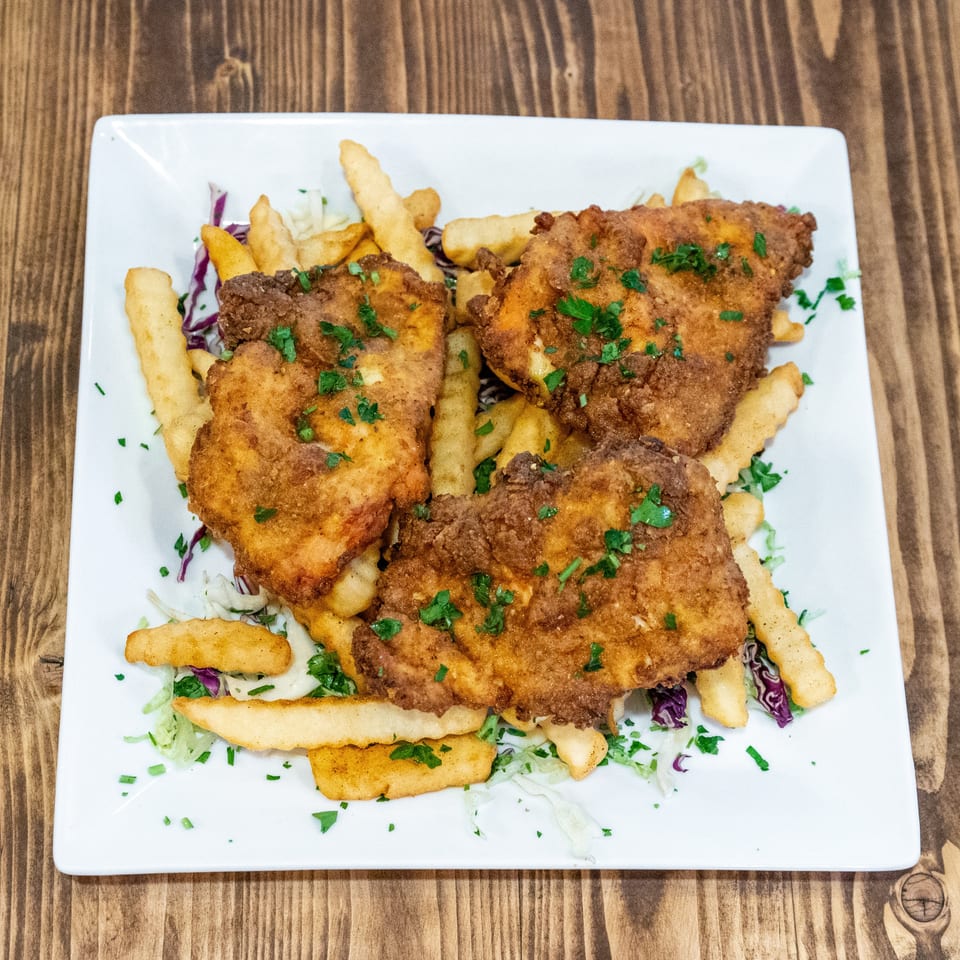 Three pieces of golden-brown fried chicken, french fries, and shredded cabbage on a white plate.