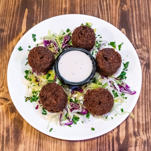 Five falafel balls arranged around a small bowl of white sauce on a bed of shredded lettuce.