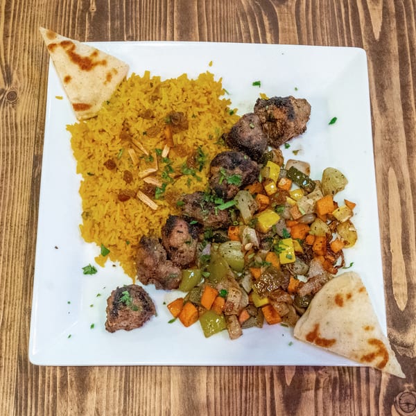 A white plate with yellow rice, grilled meat, mixed vegetables, and two pieces of flatbread.