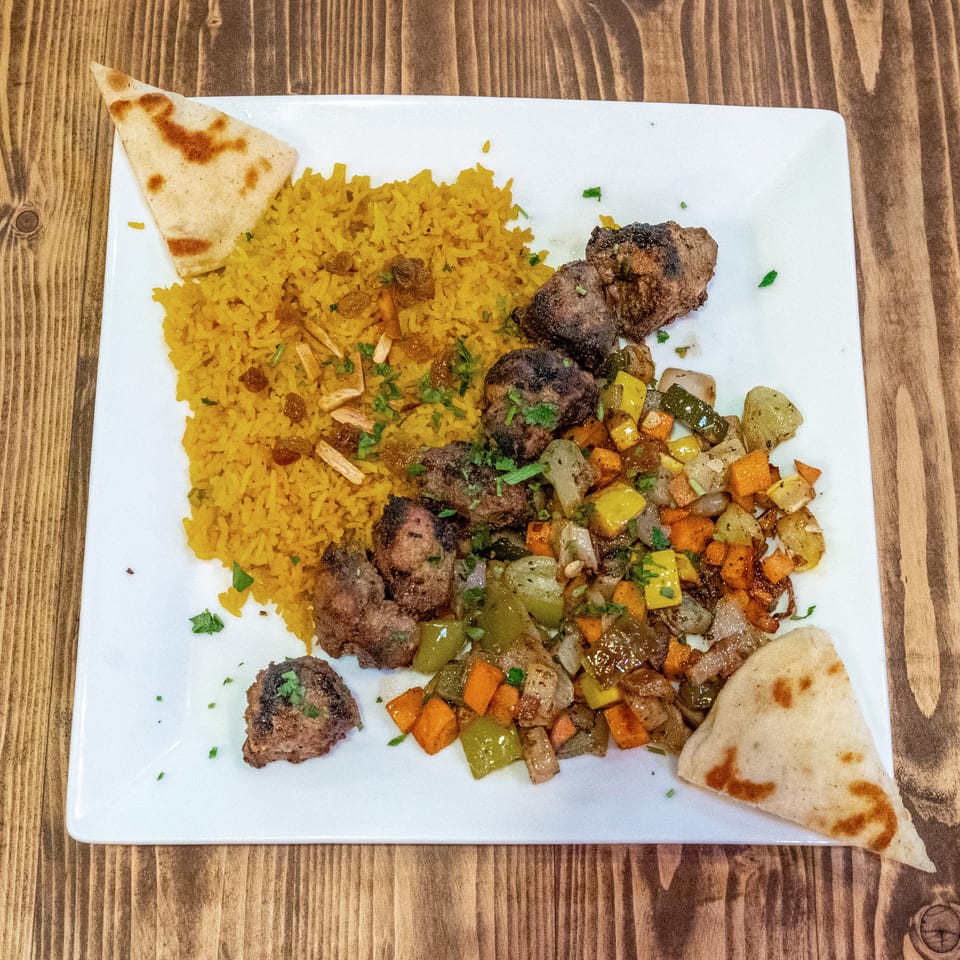 A white plate with yellow rice, grilled meat, mixed vegetables, and two pieces of flatbread.