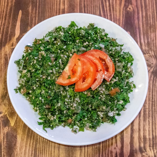 Tabbouleh salad with chopped parsley, bulgur, and three tomato slices on a white plate.