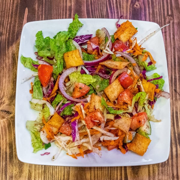 A vibrant salad with lettuce, red onions, tomatoes, shredded carrots, and toasted pita bread.
