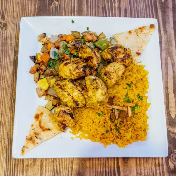 Grilled chicken pieces, yellow rice, roasted vegetables, and pita bread on a white plate.