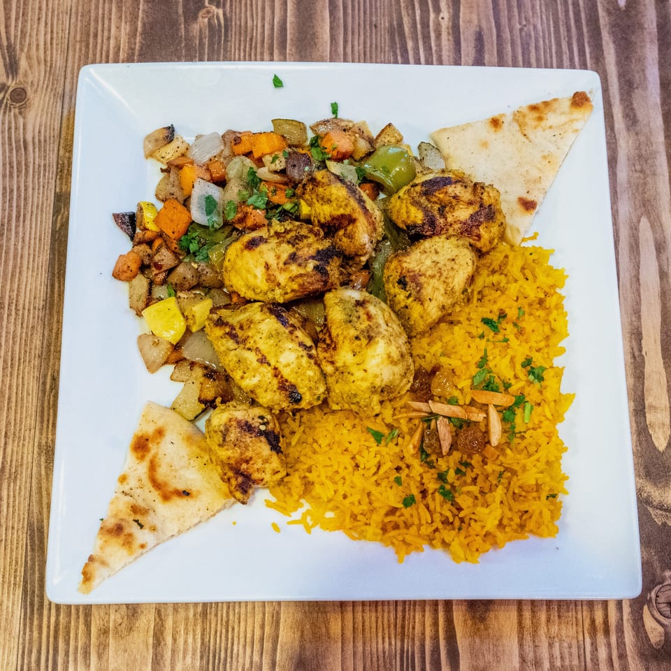 Grilled chicken pieces, yellow rice, roasted vegetables, and pita bread on a white plate.