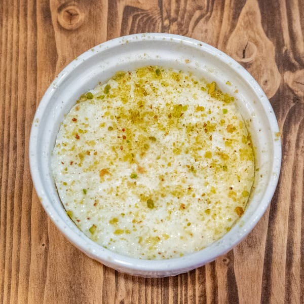 Creamy white dessert in a round white bowl, topped with green and red sprinkles on a wooden table.