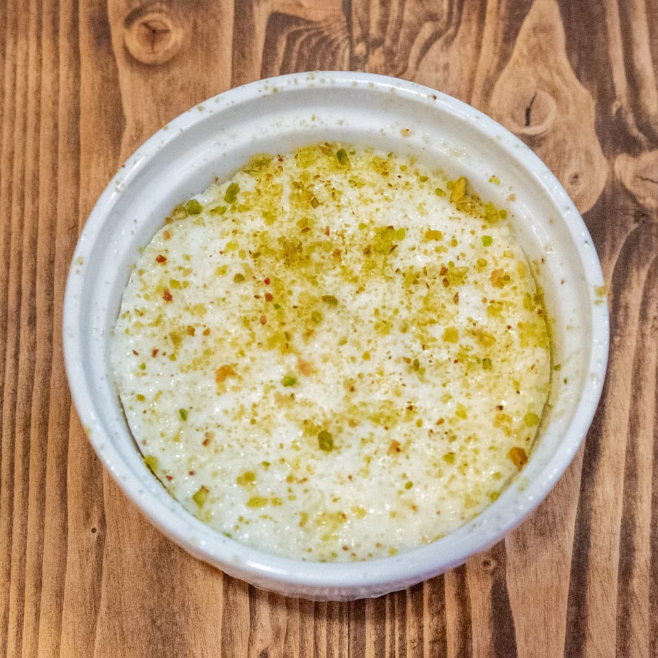 Creamy white dessert in a round white bowl, topped with green and red sprinkles on a wooden table.